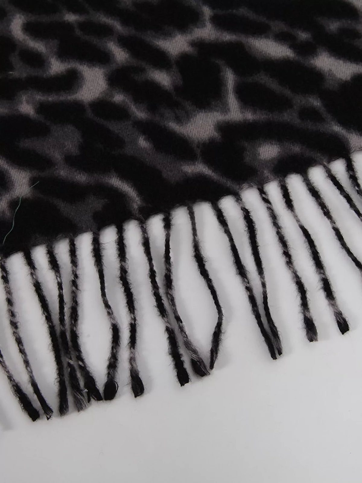 Black leopard print scarf with long fringe along the bottom edge.