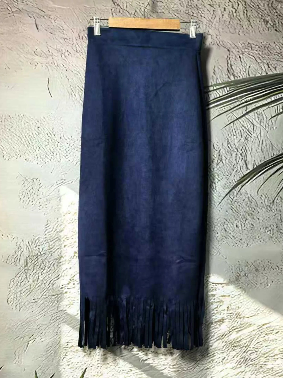 Dark blue midi skirt with a straight silhouette and fringe hem, hanging on a clip hanger.