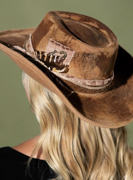 Taupe western hat worn with wide brim, distressed felt and patch with metal ornament