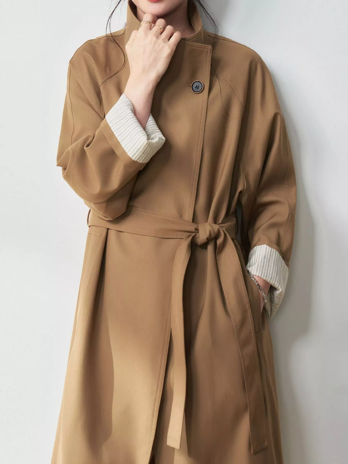 Khaki coat detail showing the asymmetric closure, dark button, and waist belt