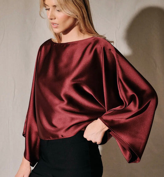 Burgundy satin poncho top with boat neck and draped dolman sleeves, angled front view