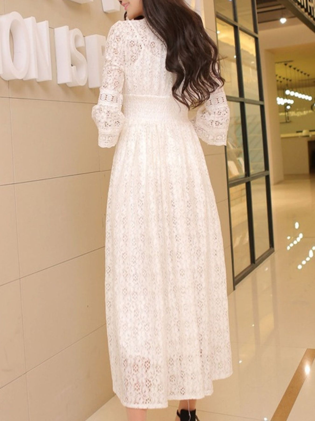 Back view of a white lace midi dress with a fitted waist and flared sleeves