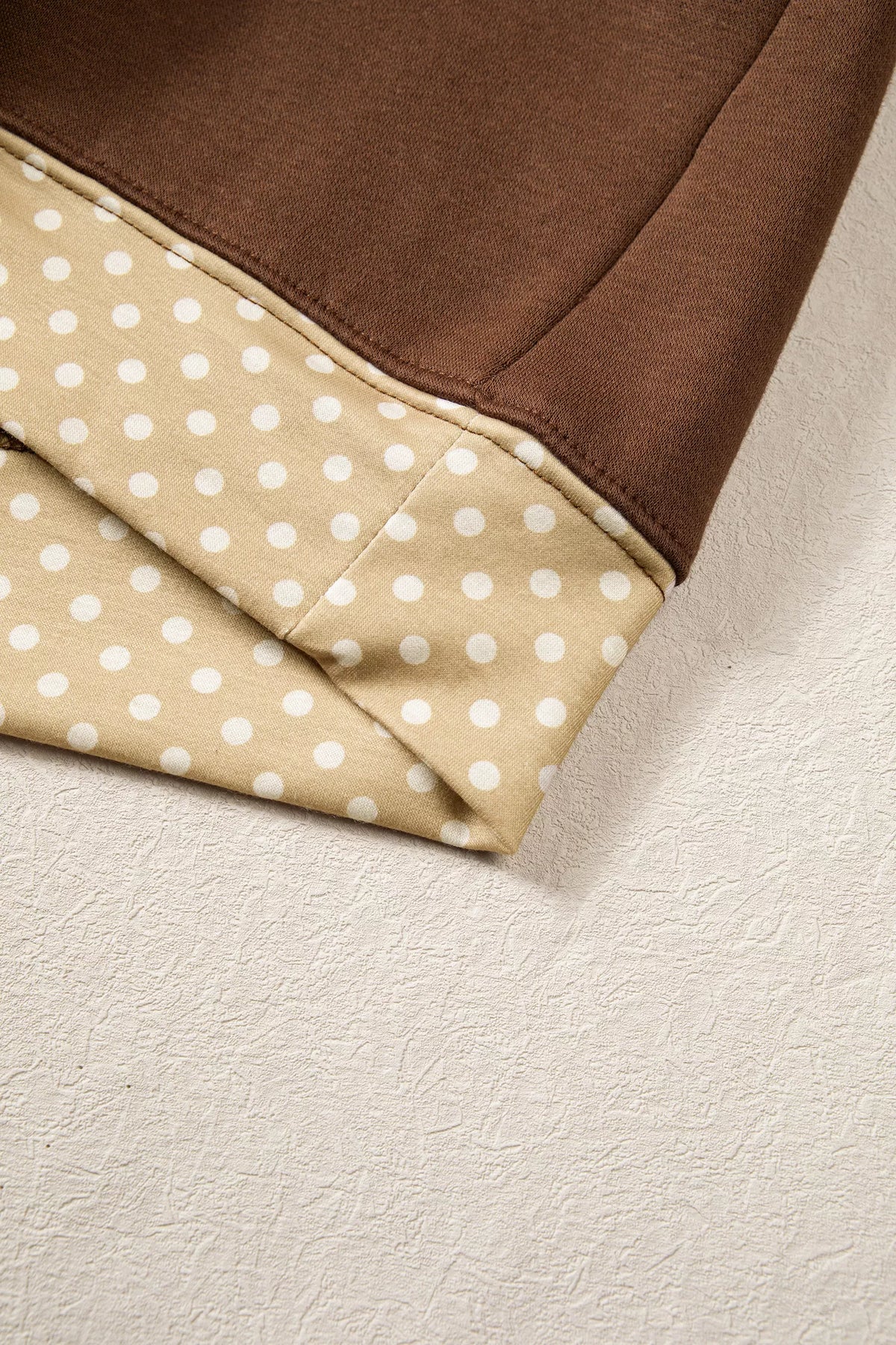 Polka-dot trimmed cuff hem detail on a dark brown sweatshirt sleeve