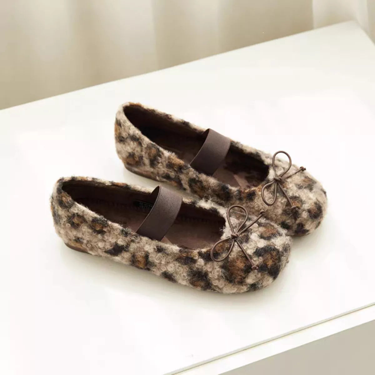 Brown leopard print faux fur slip-on shoes with black ribbon straps and bow eyelets