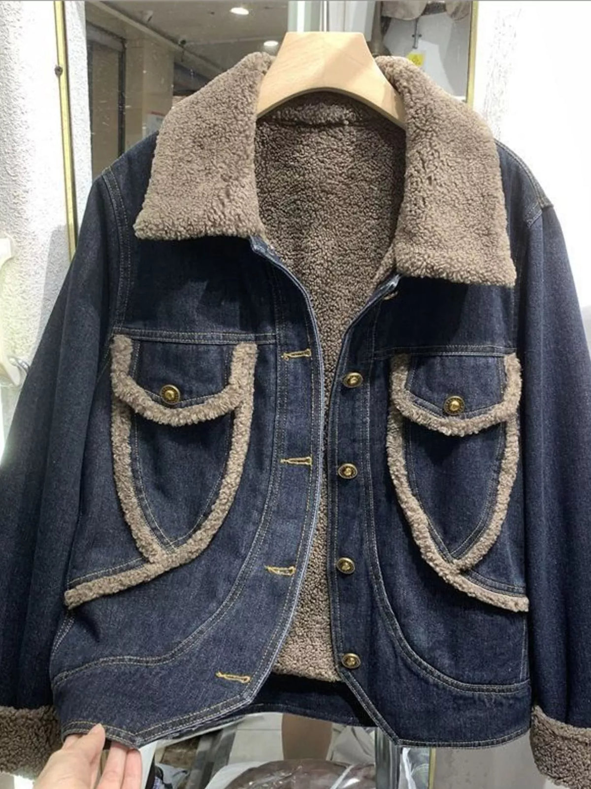 Dark blue denim jacket with taupe sherpa lining, contrast trim, brass buttons and flap pockets