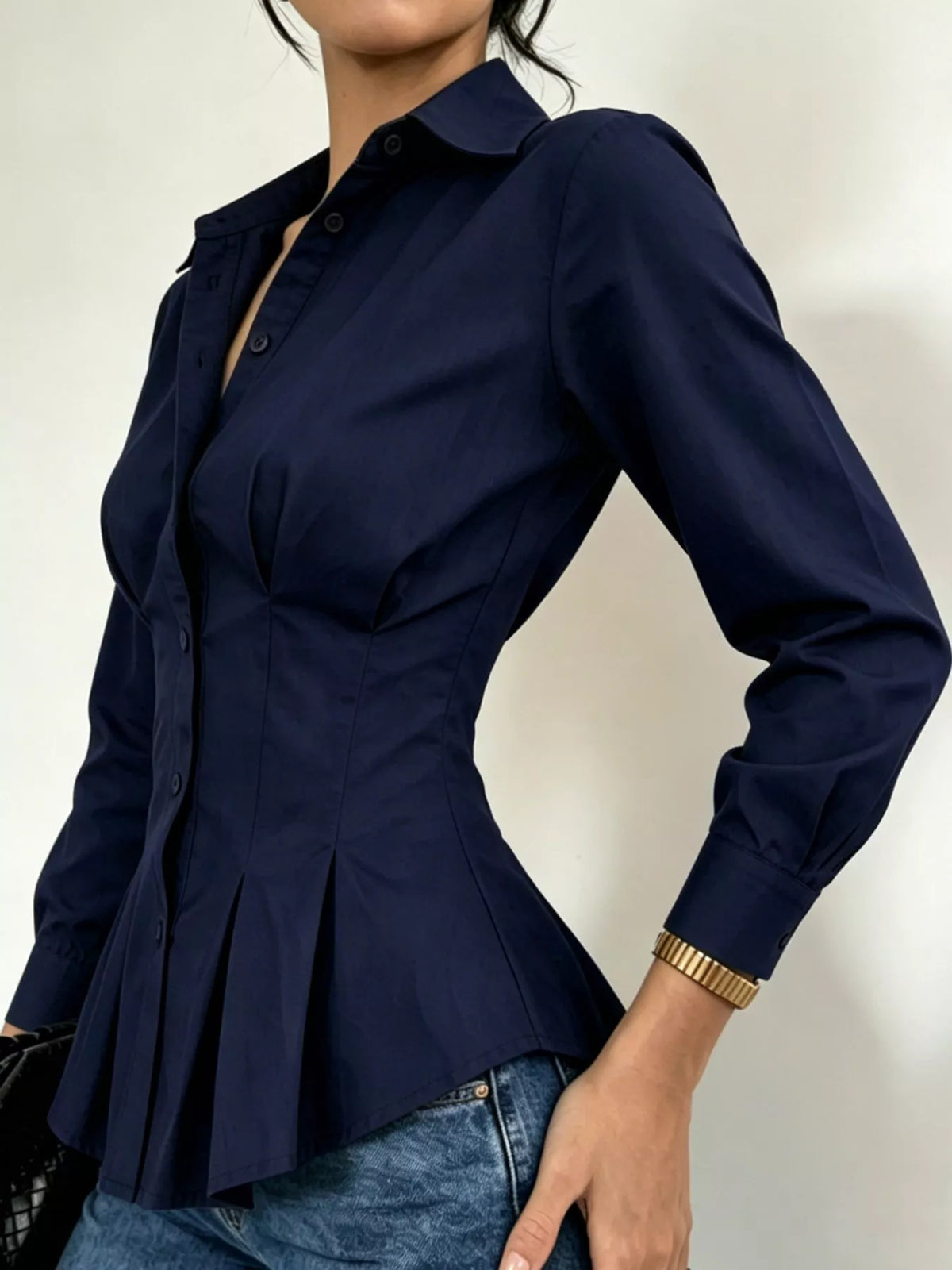 Navy button-down peplum blouse with fitted waist and long sleeves, side view