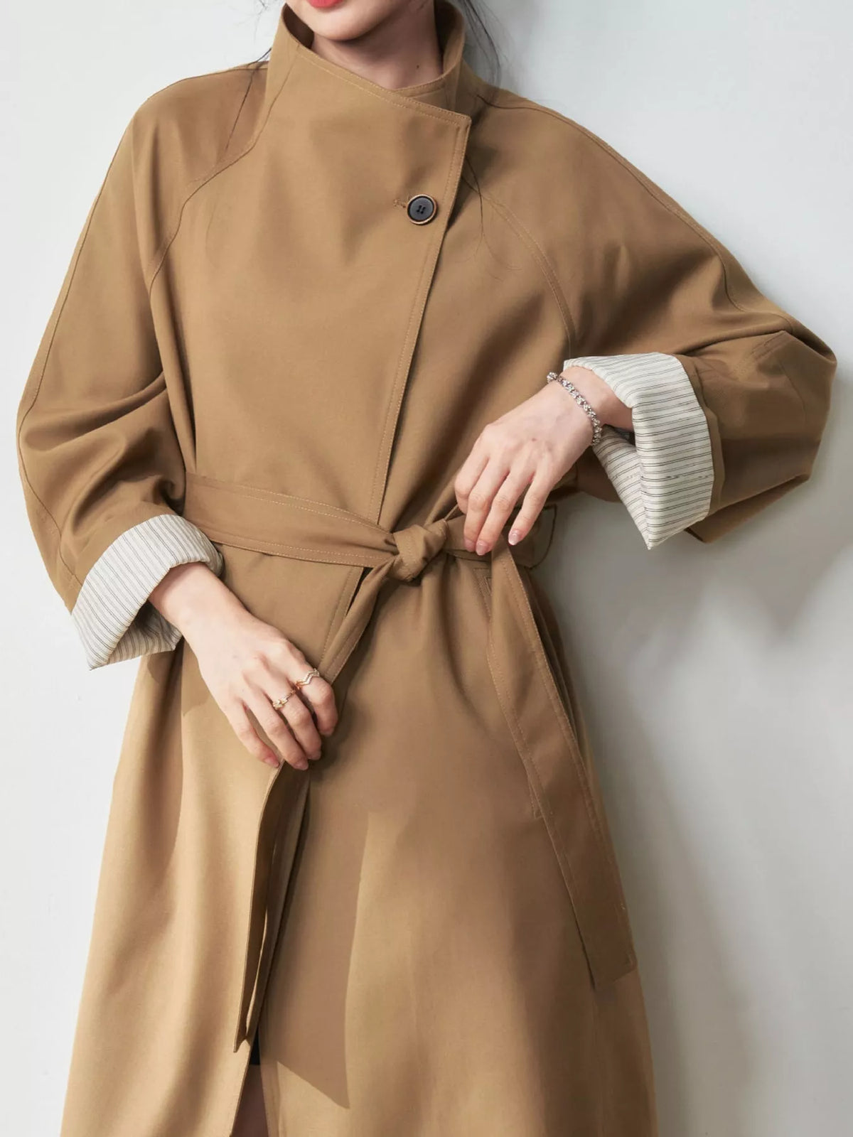 Khaki trench coat with high collar, tied belt, and contrasting ribbed cuffs
