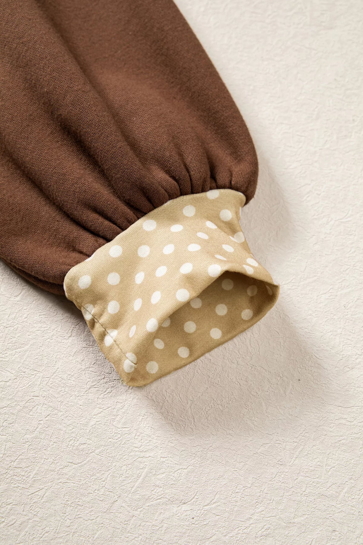 Brown sweatshirt sleeve cuff with beige polka-dot trim and stitched hem