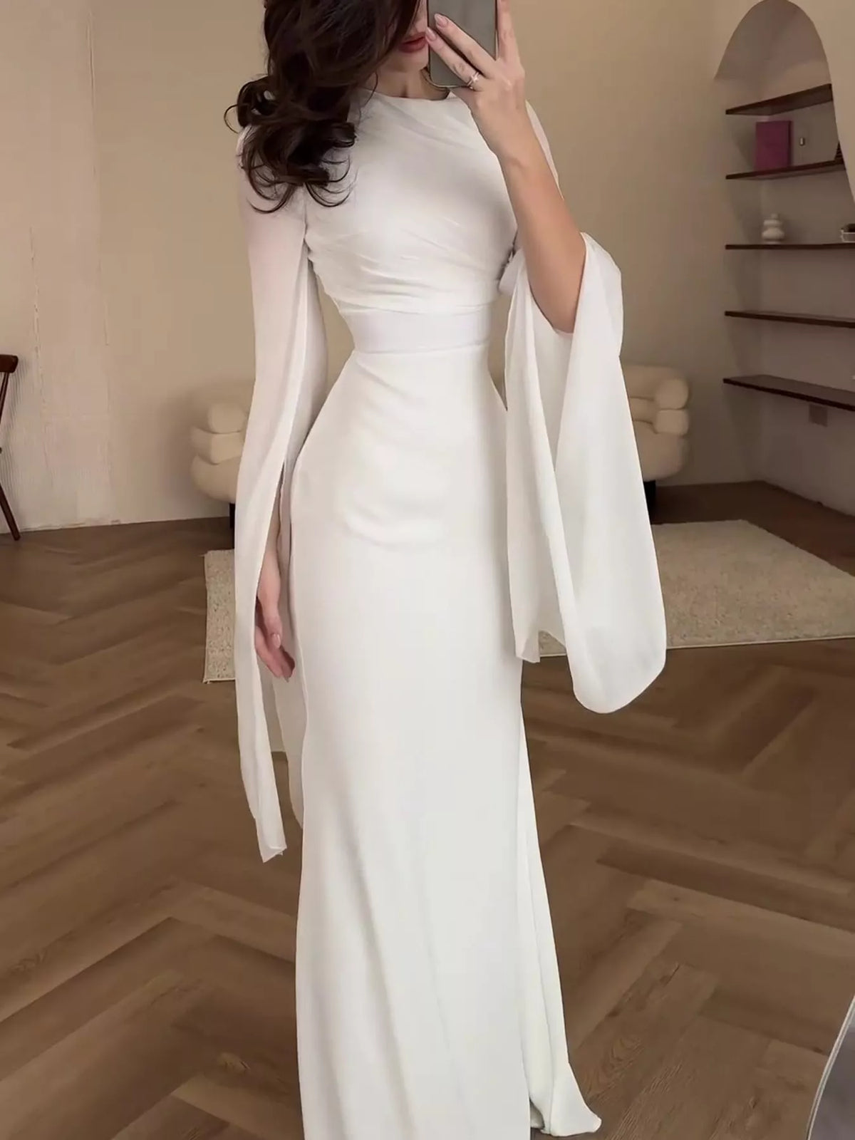 White floor-length dress with a fitted silhouette and long draped sleeves