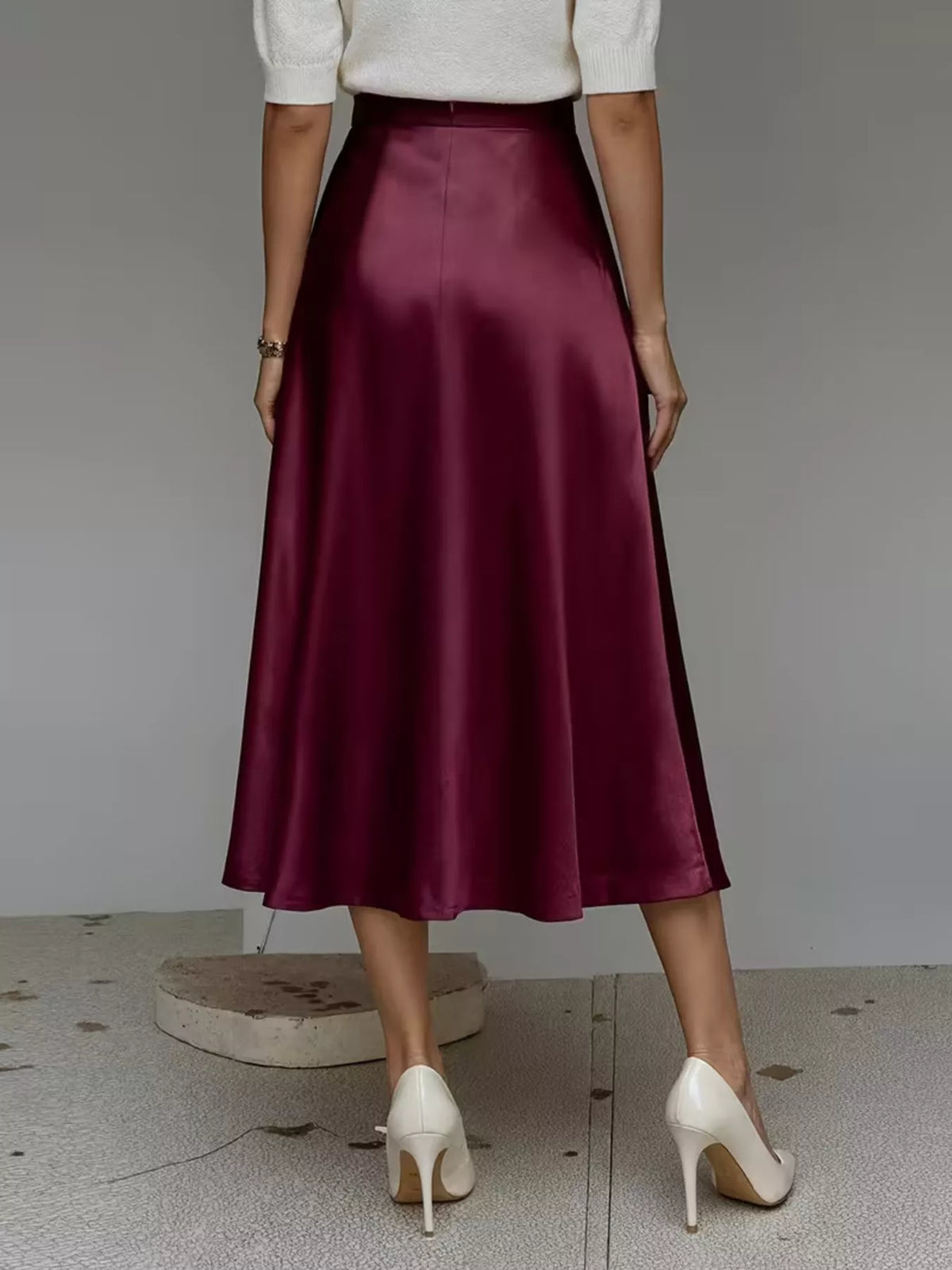 Back view of a wine red satin midi skirt with a high waist and flowing hem.
