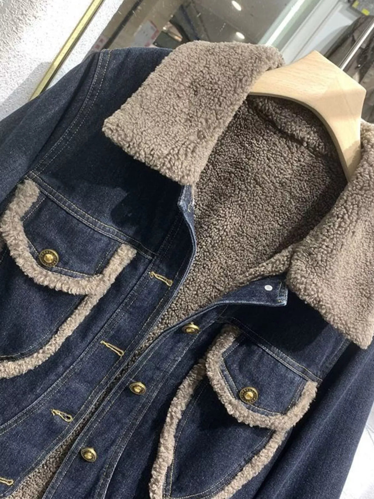 Close view of the sherpa collar, lining, contrast-trimmed pockets and brass buttons on a denim jacket