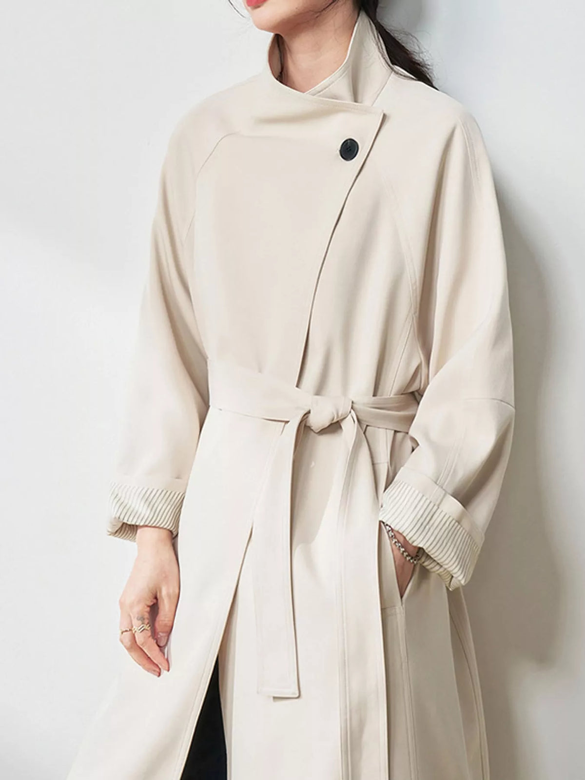 Beige trench coat with angled button closure, belted waist, and ribbed cuff lining