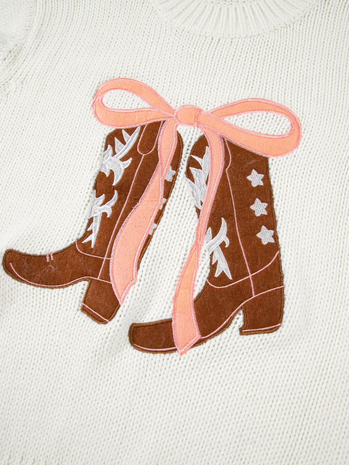 Close-up of embroidered bow boots graphic on white knit sweater