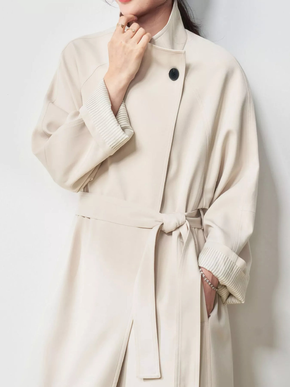 Beige trench coat detail showing a single button, belted waist, and rolled ribbed cuffs