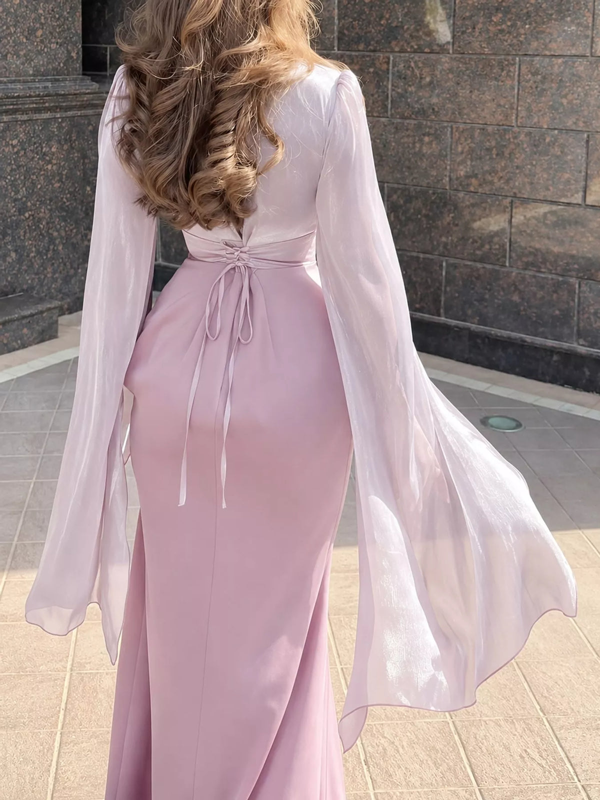 Back view of a pale pink maxi dress with tie-back waist and sheer flared sleeves