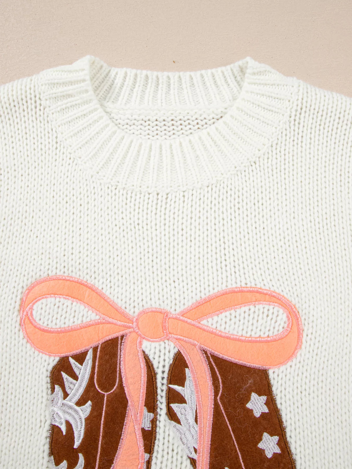 White sweater close-up of ribbed crew neckline with bow boots graphic detail