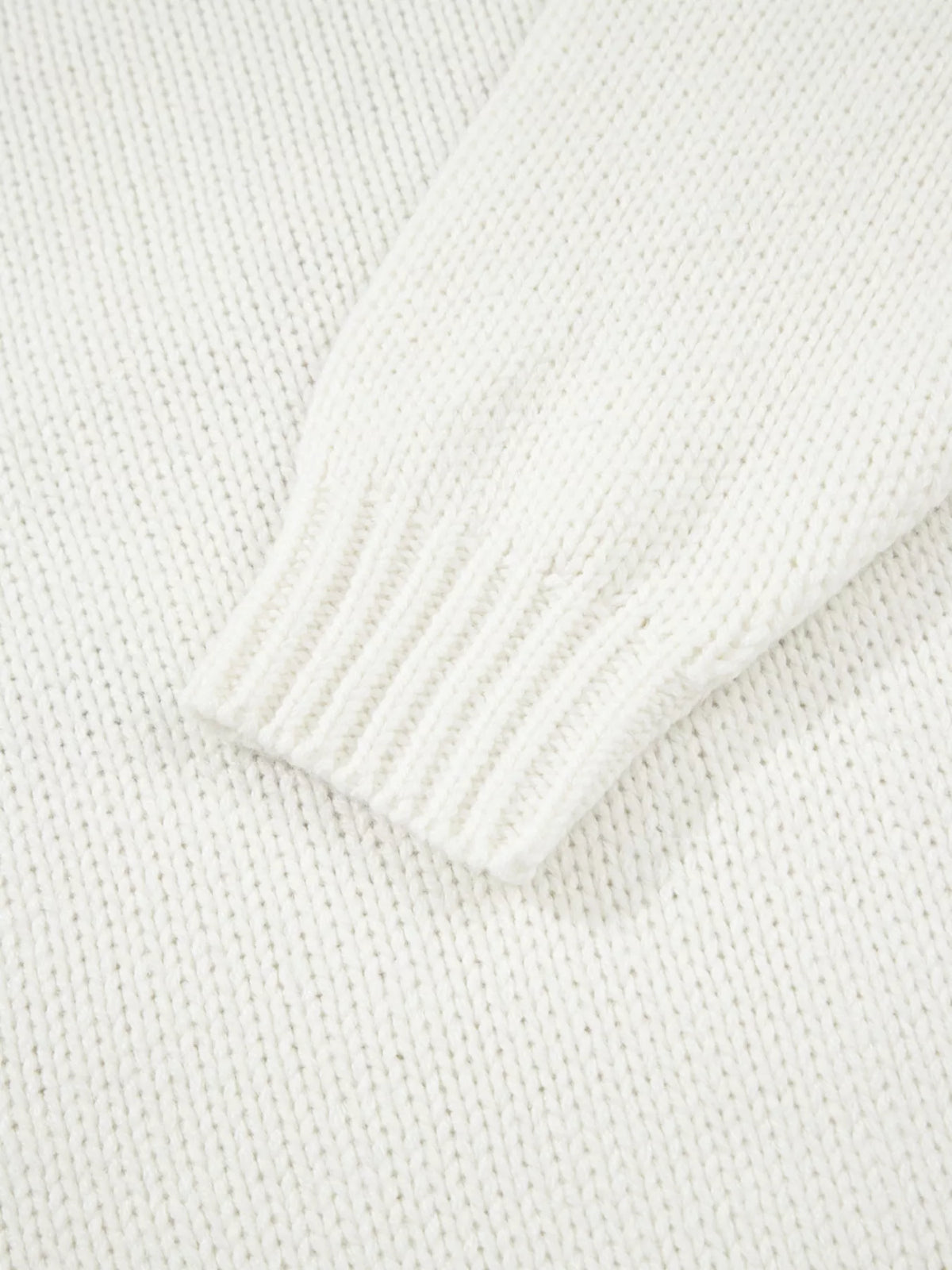 White knit sweater sleeve close-up with ribbed cuff and textured knit fabric