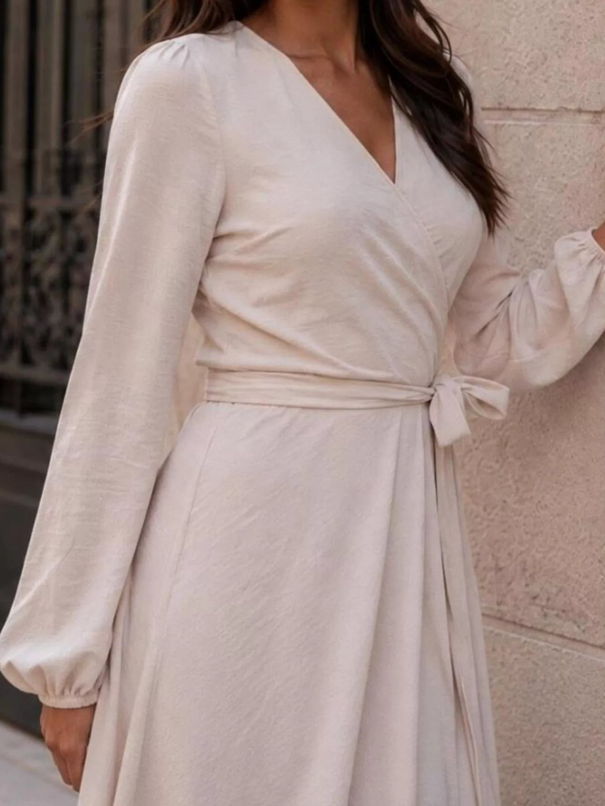 Light beige long-sleeve wrap dress detail: V-neck, gathered waist, flowing skirt.