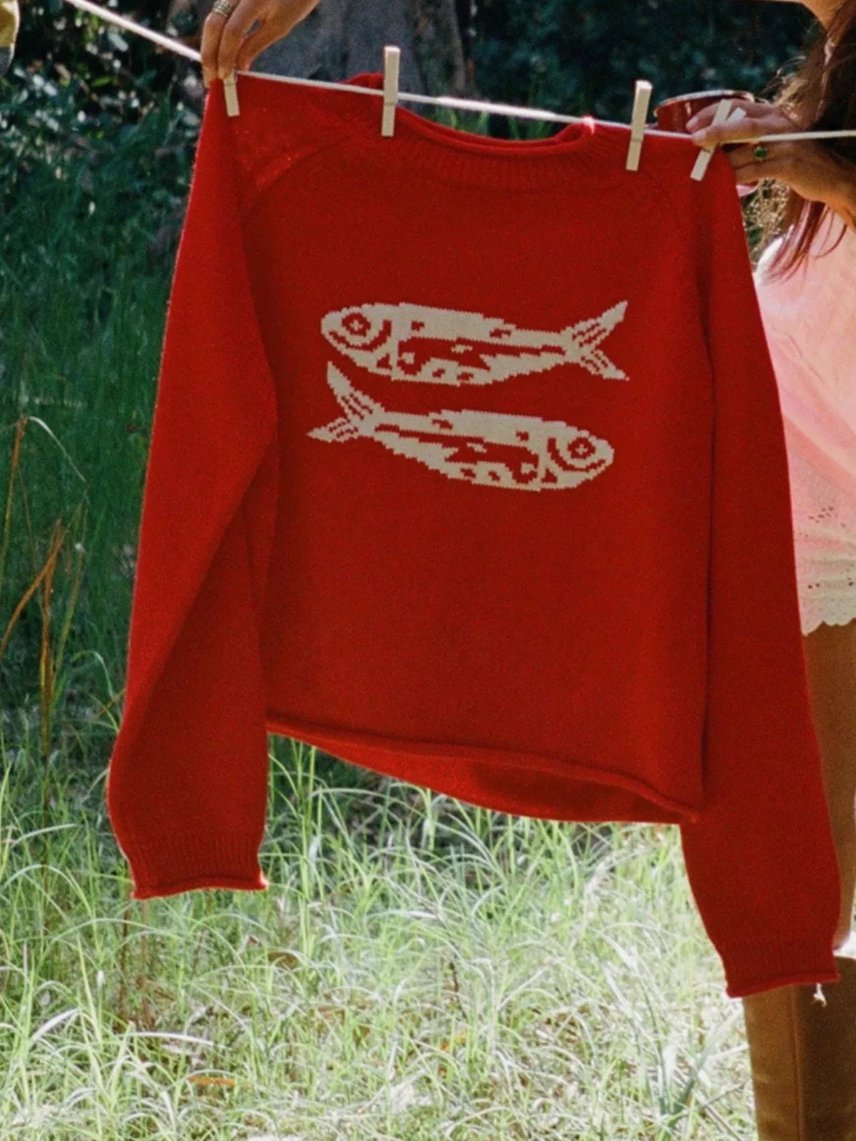 Red crew neck sweater with white fish motif, shown hanging outdoors