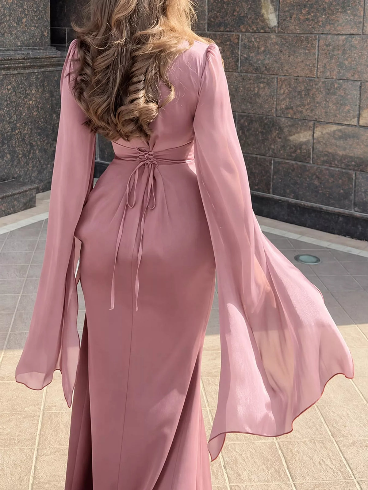 Back view of a dusty rose maxi dress with tie-back waist and sheer flared sleeves