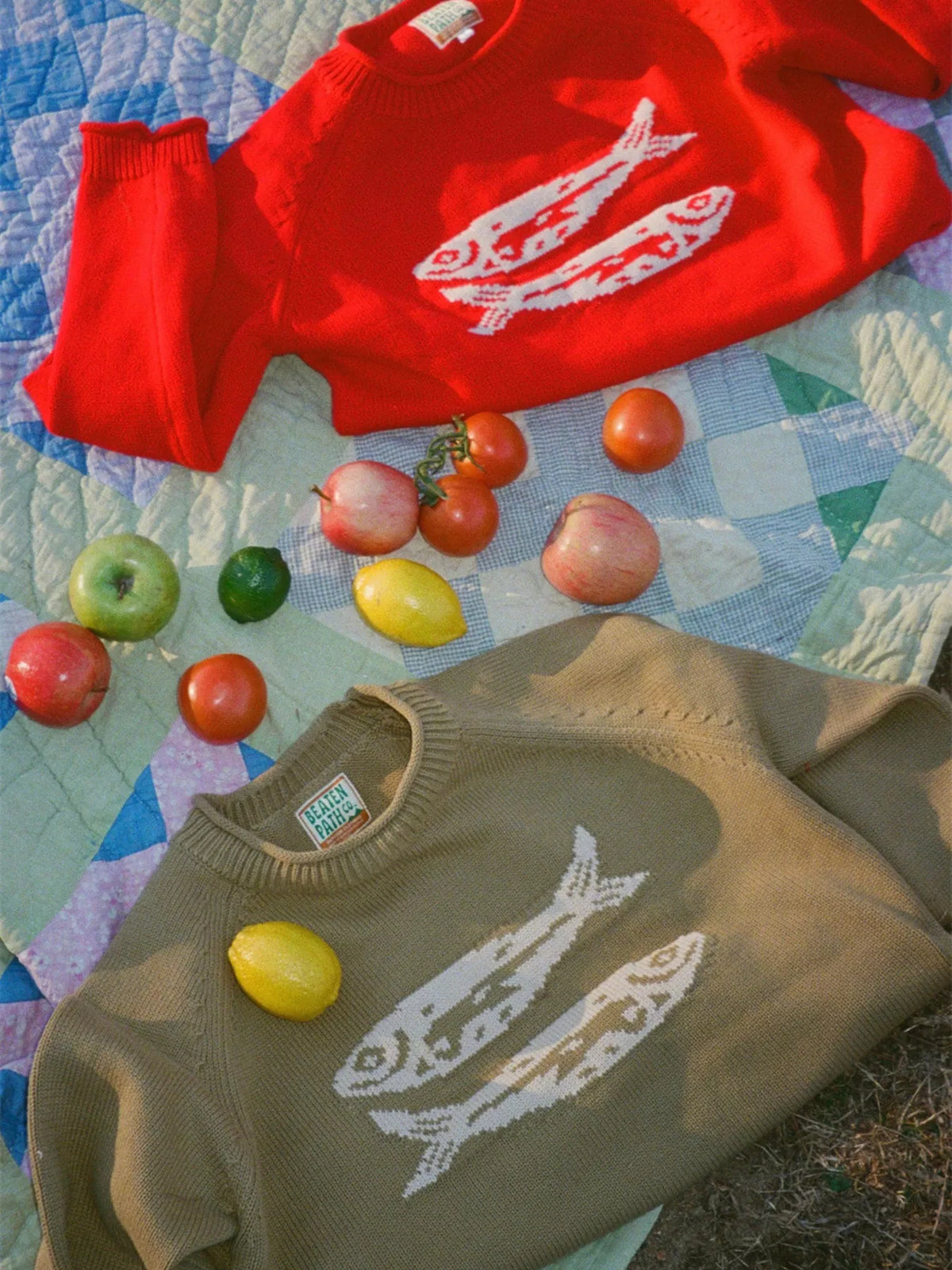 Red crew neck sweater and olive knit sweater with white fish motifs, flat lay
