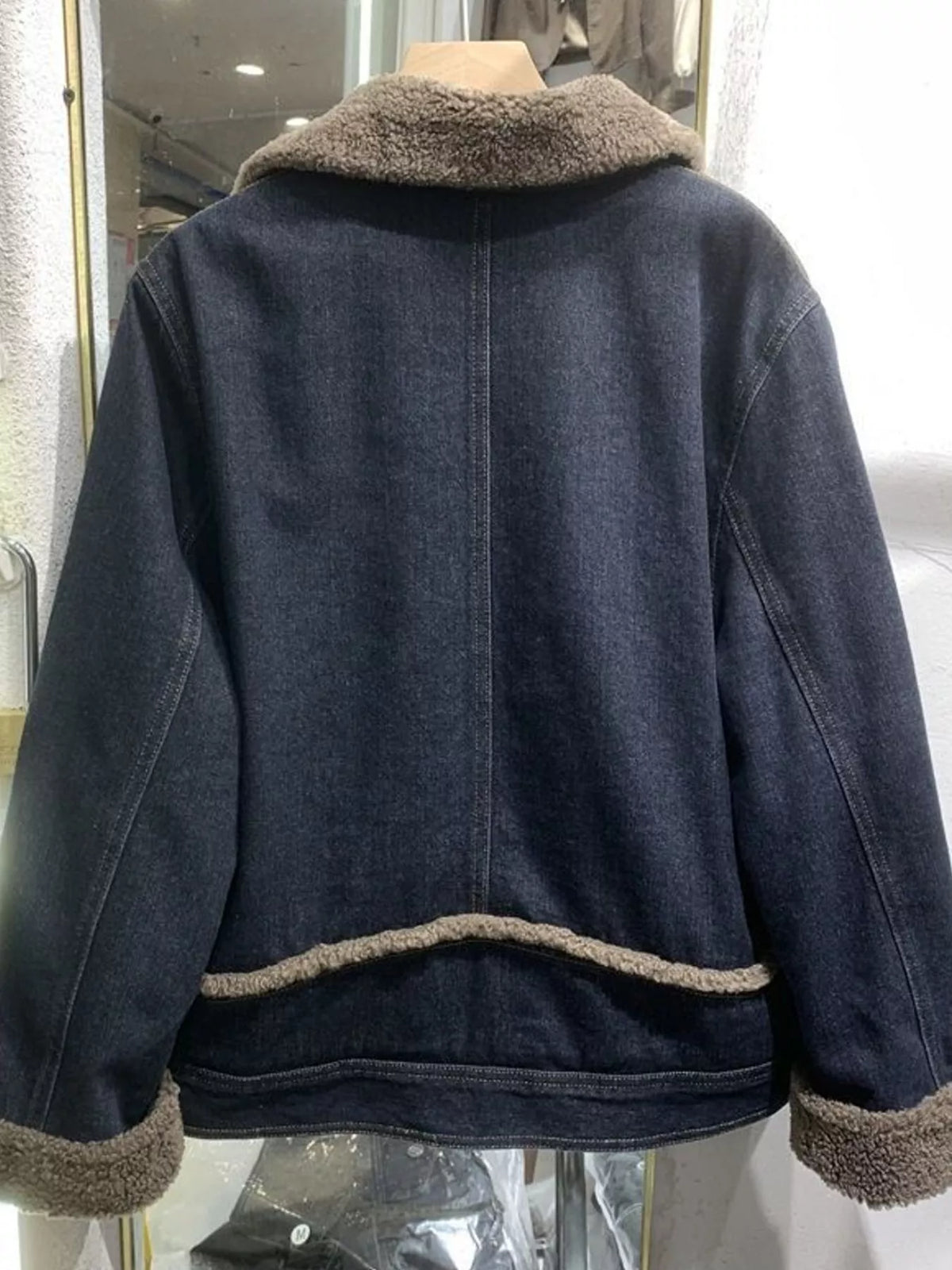 Back of a dark blue denim jacket with sherpa collar, cuffs and hem trim